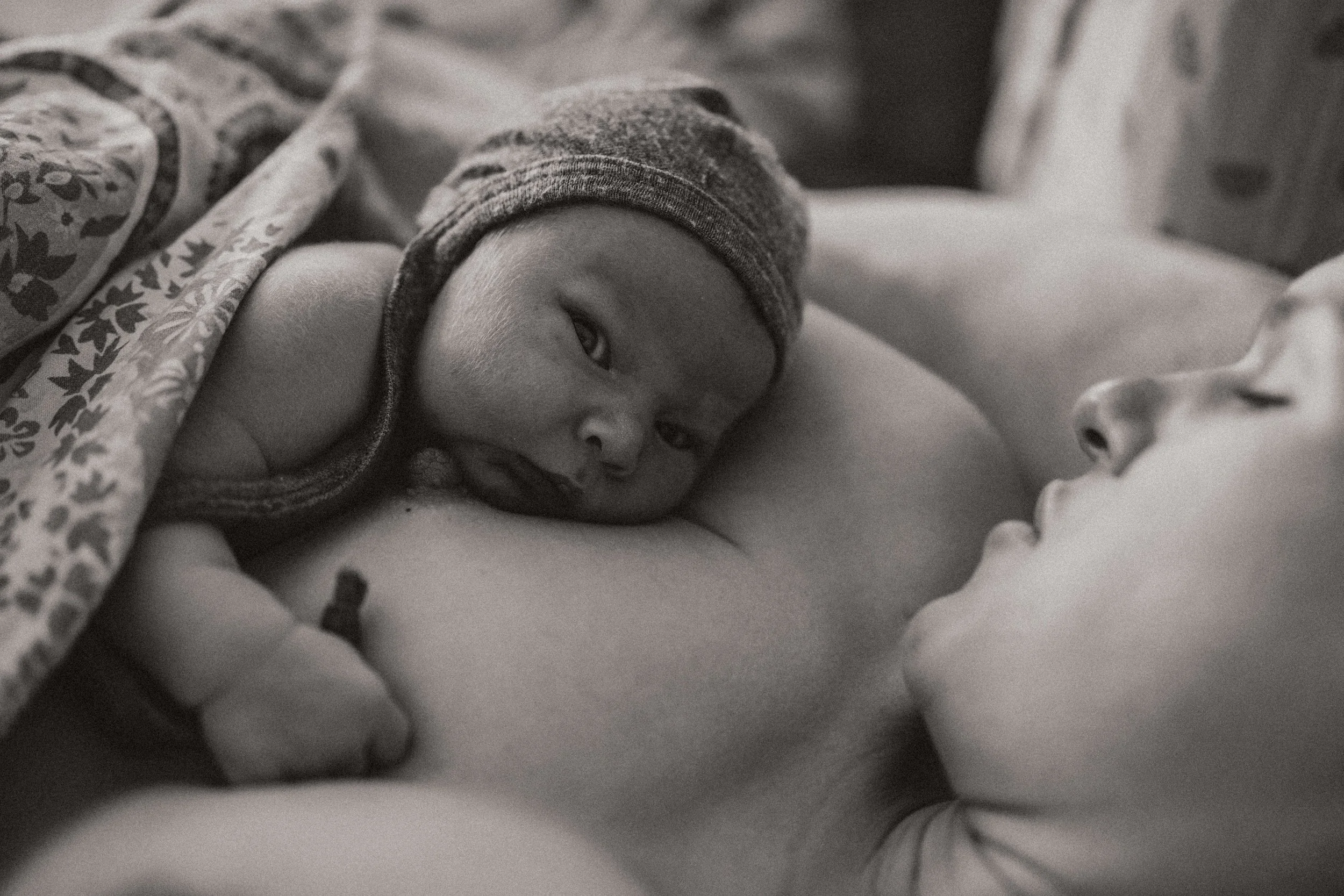 schwarz weiß bild von neugeborenen auf brust der mama liegend und in die kamera schauend