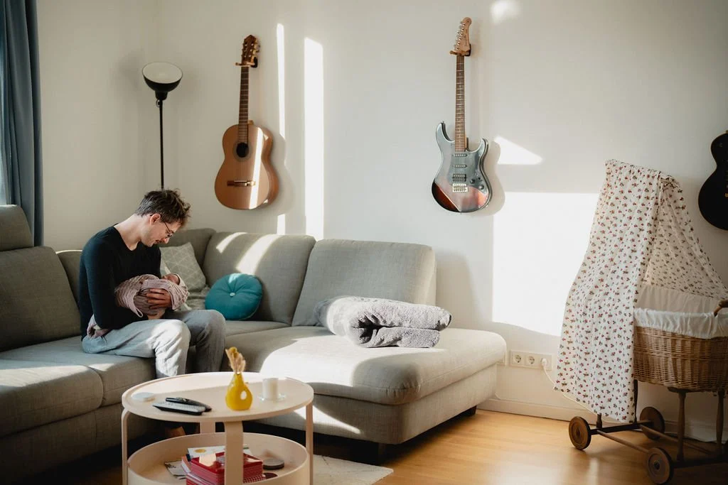 Vater hält Neugeborenes auf dem Sofa, Papa-Baby-Bonding dokumentarisch fotografiert