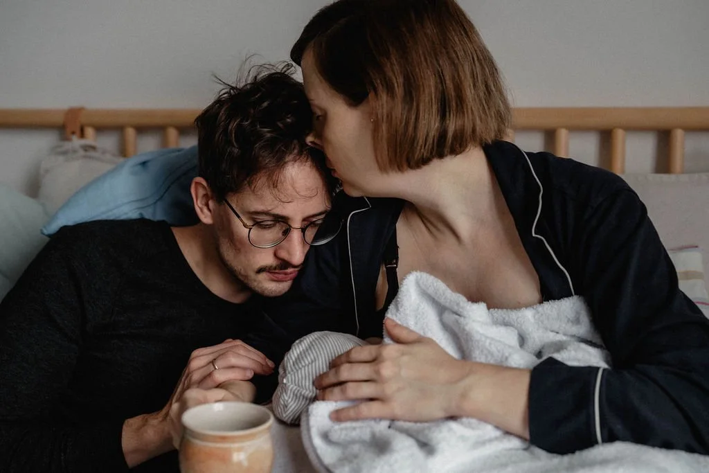 Eltern kuscheln mit Neugeborenem im Bett, erste Familienmomente im Wochenbett Berlin