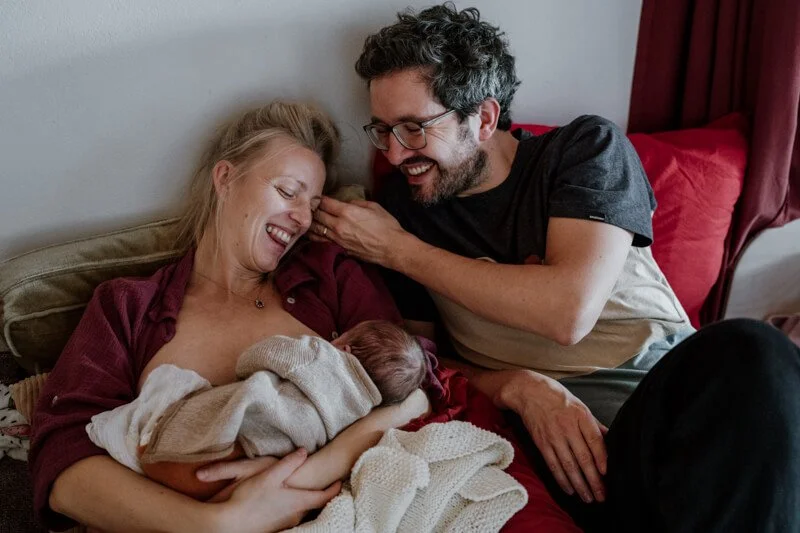 Mama und Papa liegen mit baby im bett und lachen überglücklich