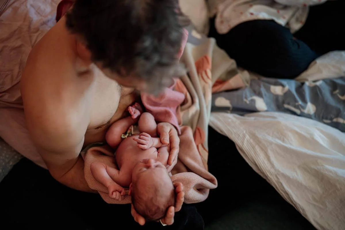 Papa hält baby in dem Arm im Bett sitztend. Haut an Haut.