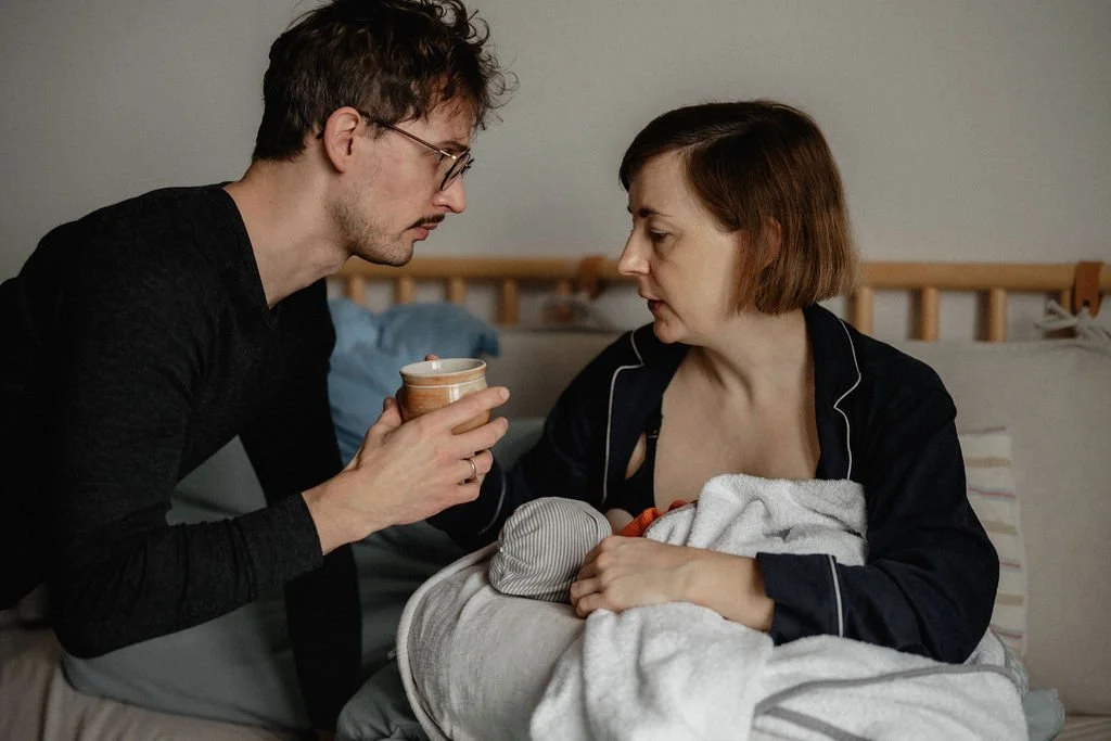 Vater reicht stillender Mutter Getränk im Wochenbett, Fürsorge dokumentarisch festgehalten