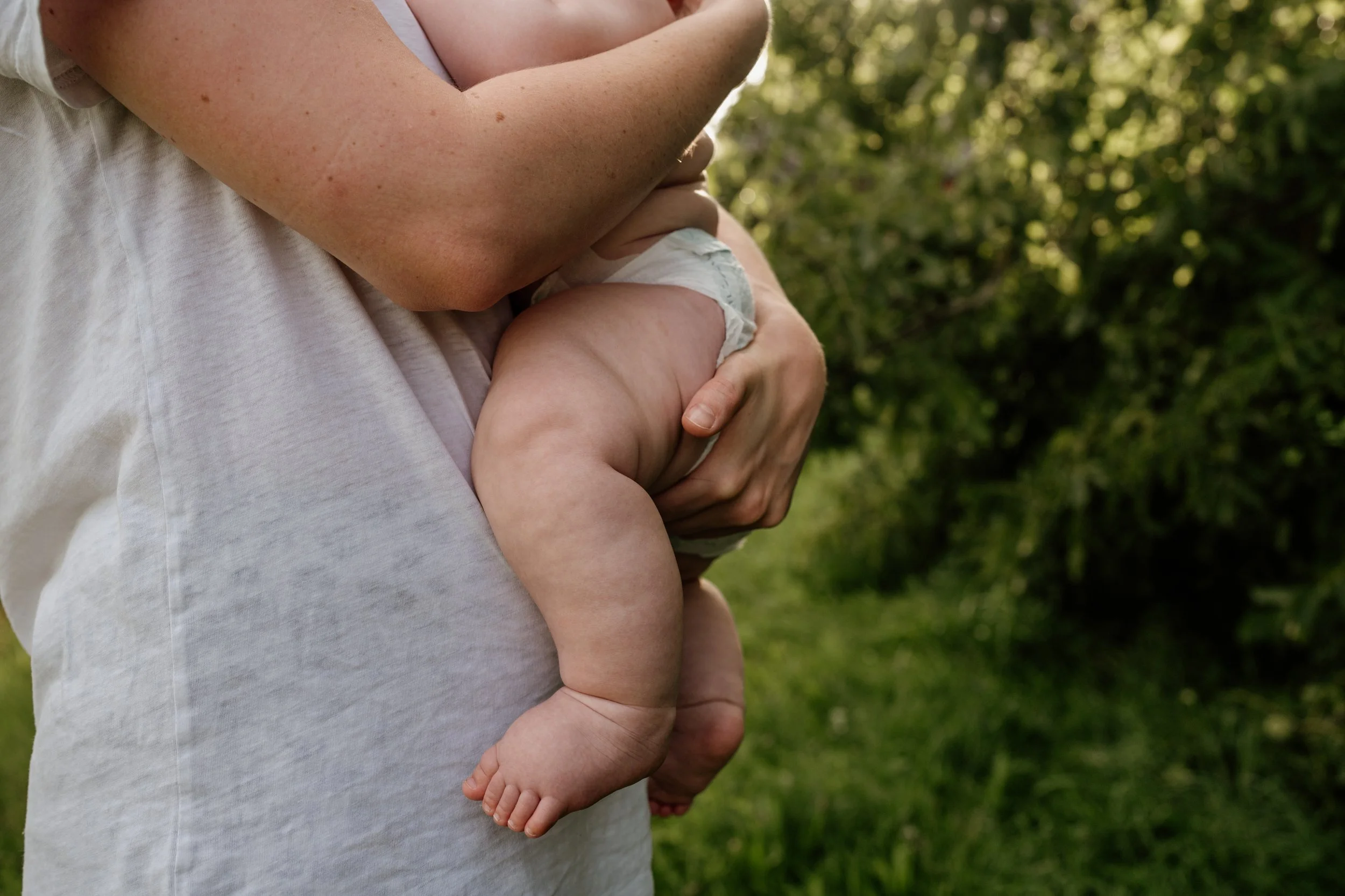Mama haelt Baby auf Arm mit speckigen Babybeinen
