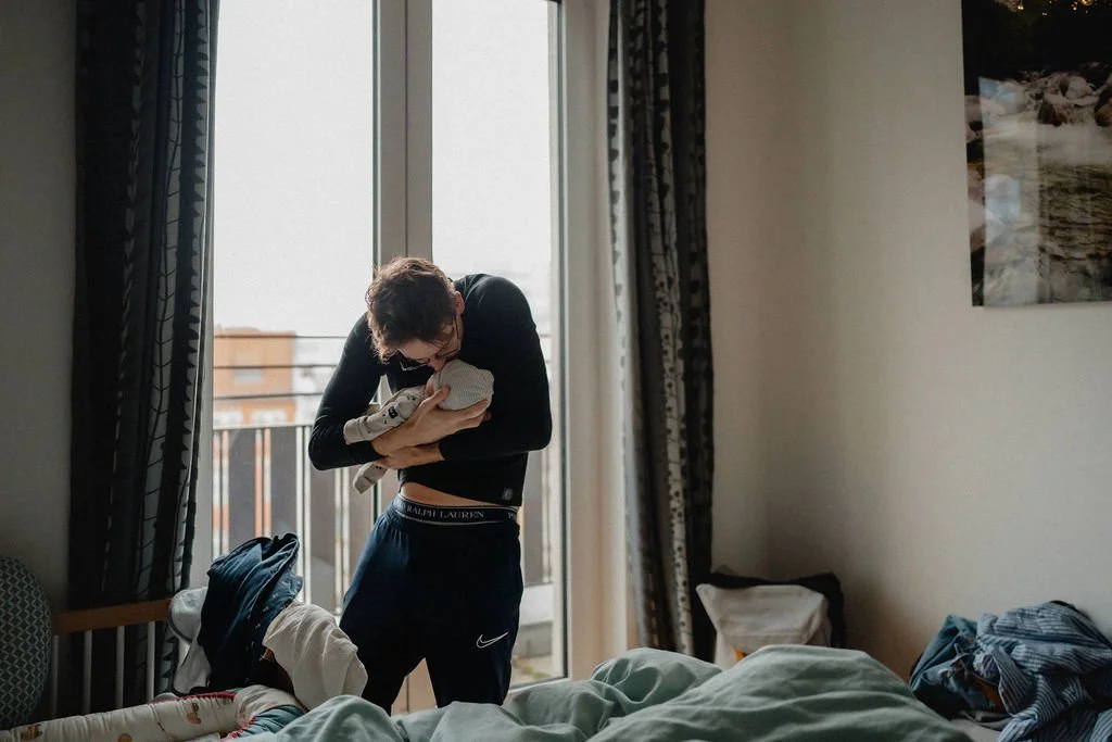 Vater küsst Neugeborenes zärtlich im Wochenbett, emotionale Babyfotografie zuhause