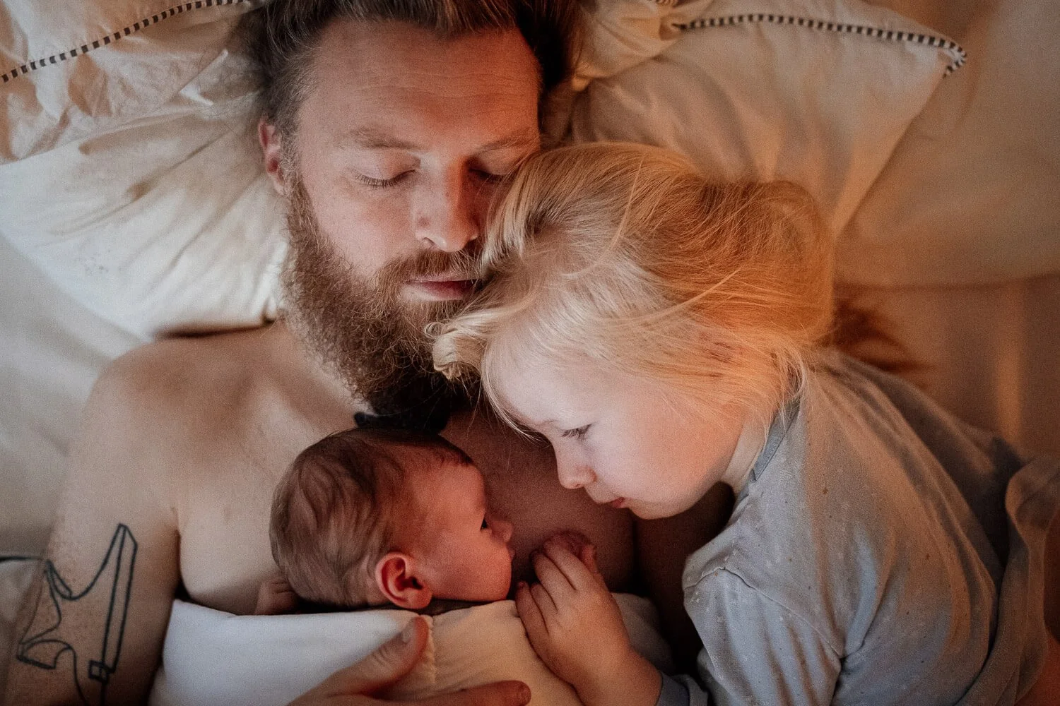 Neugeborenes und Bruder liegen auf schlafenden Papa und schauen sich in die Augen