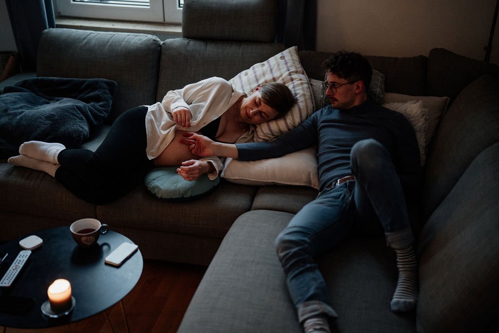 Paar liegt gemeinsam entspannt auf dem Sofa, ungestellte Homestory Schwangerschaft