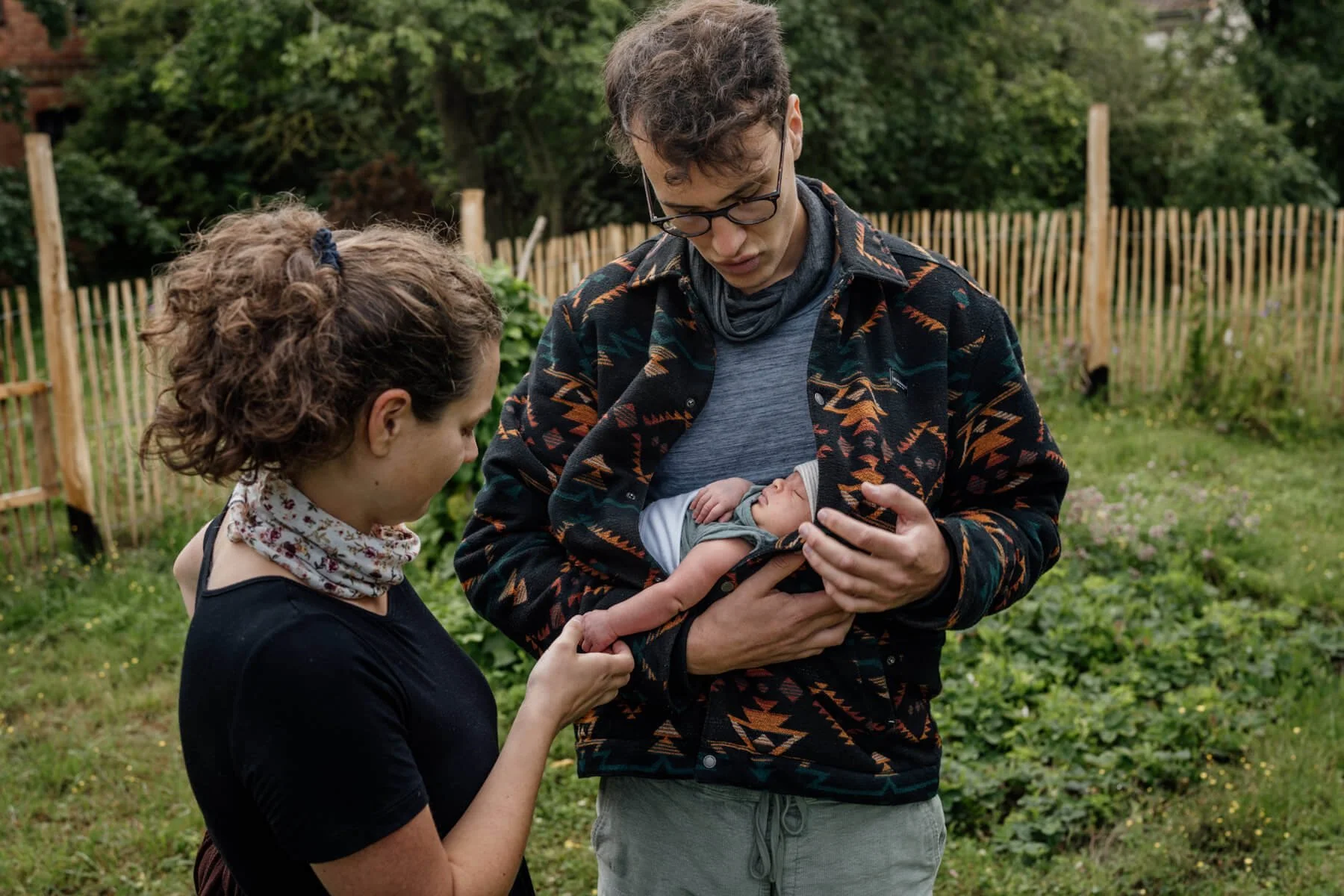 Vater hält baby unter der Jacke im Garten und mama hält die Hand vom Baby