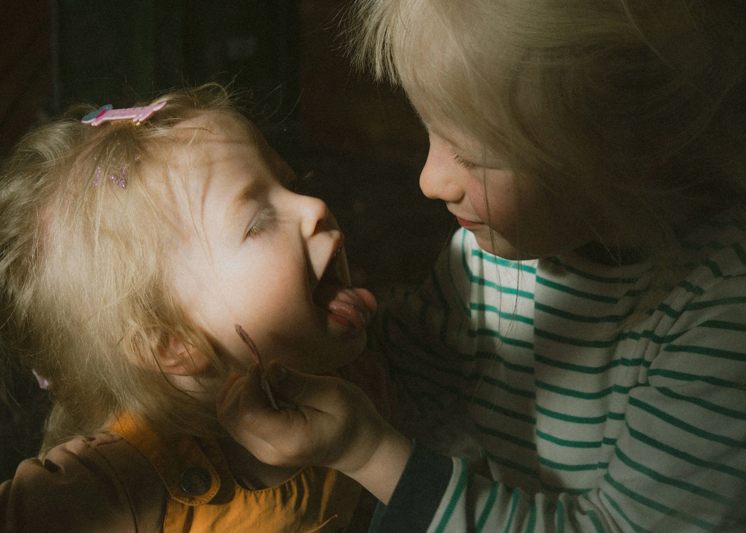 Geschwister schauen sich an. Nahaufnahme und die Schwester streckt dem Bruder die zunge raus in dunkler umgebung.