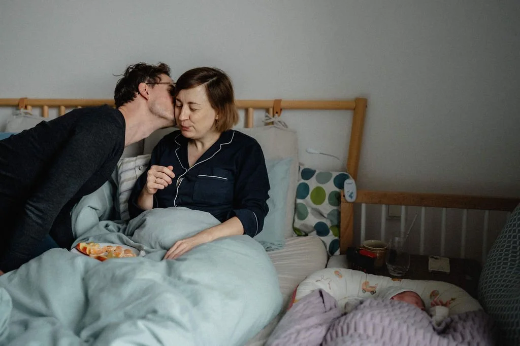 Vater küsst stillende Mutter im Wochenbett, Liebe und Fürsorge dokumentarisch fotografiert
