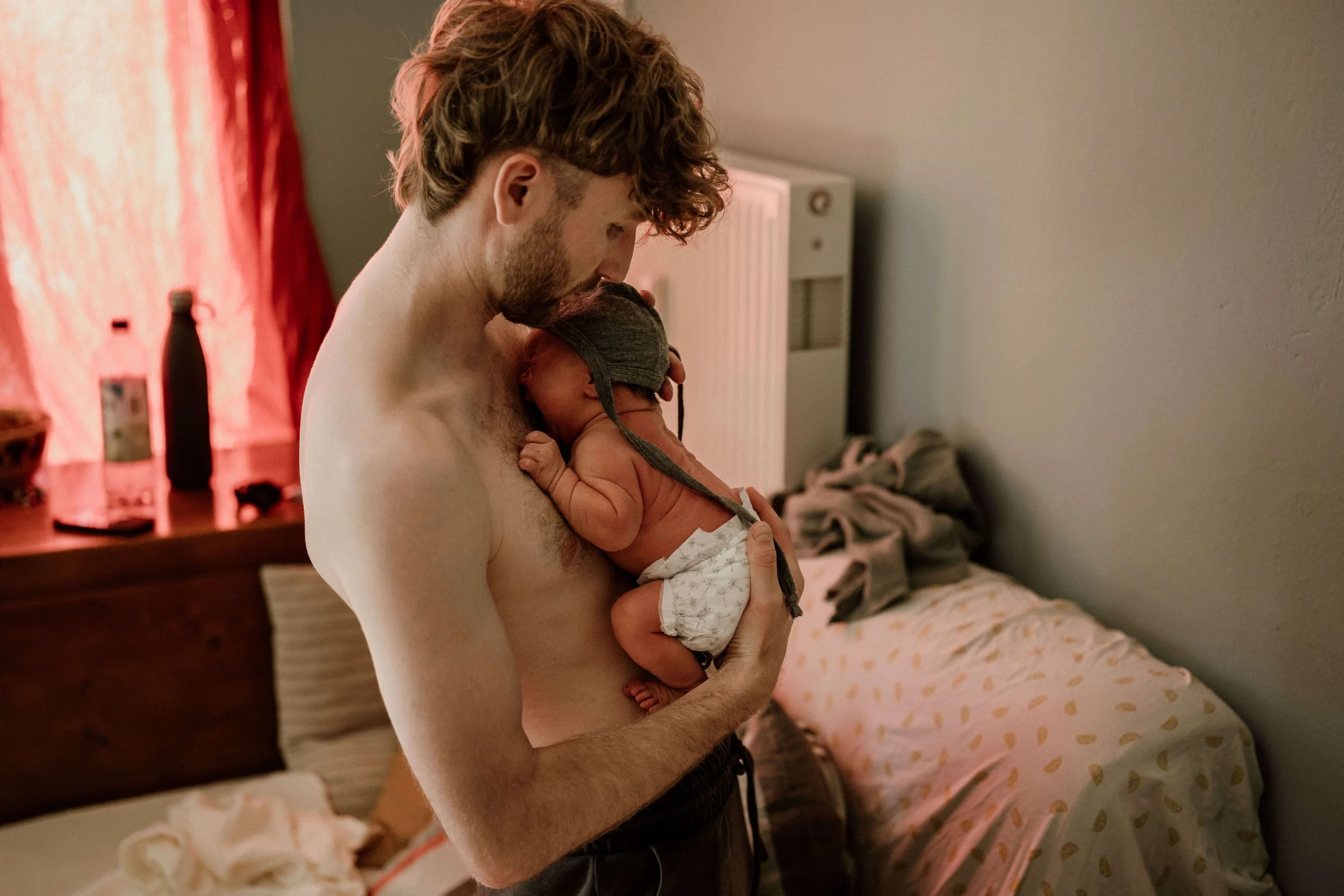 Papa haelt Baby Haut an Haut und troestet es im Wochenbett