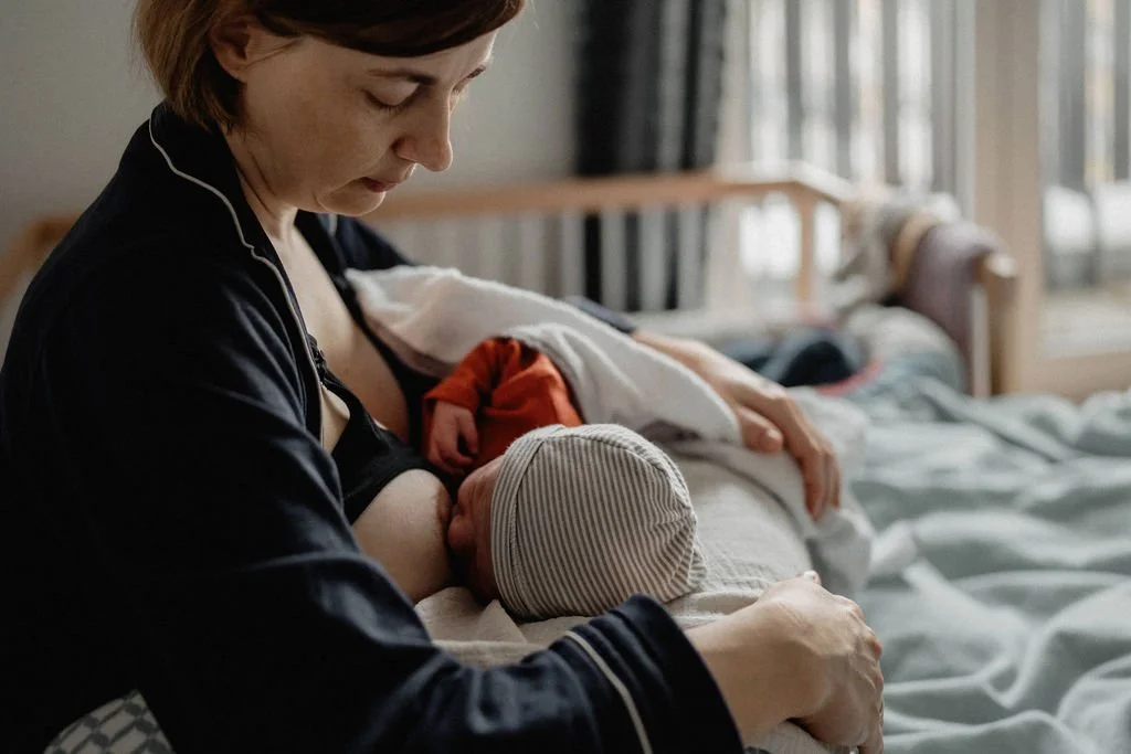 Mutter stillt Baby im Bett, Hautkontakt Wochenbett, dokumentarische Neugeborenenfotografie