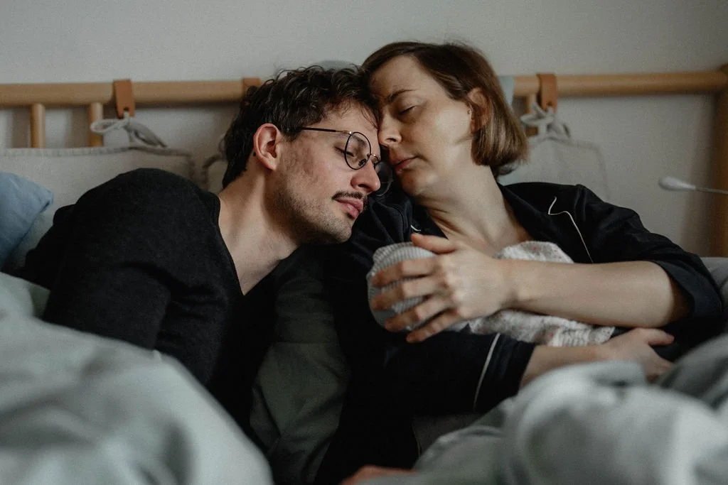 Erschöpfte Eltern mit Neugeborenem im Wochenbett, ehrliche Wochenbettfotografie Berlin