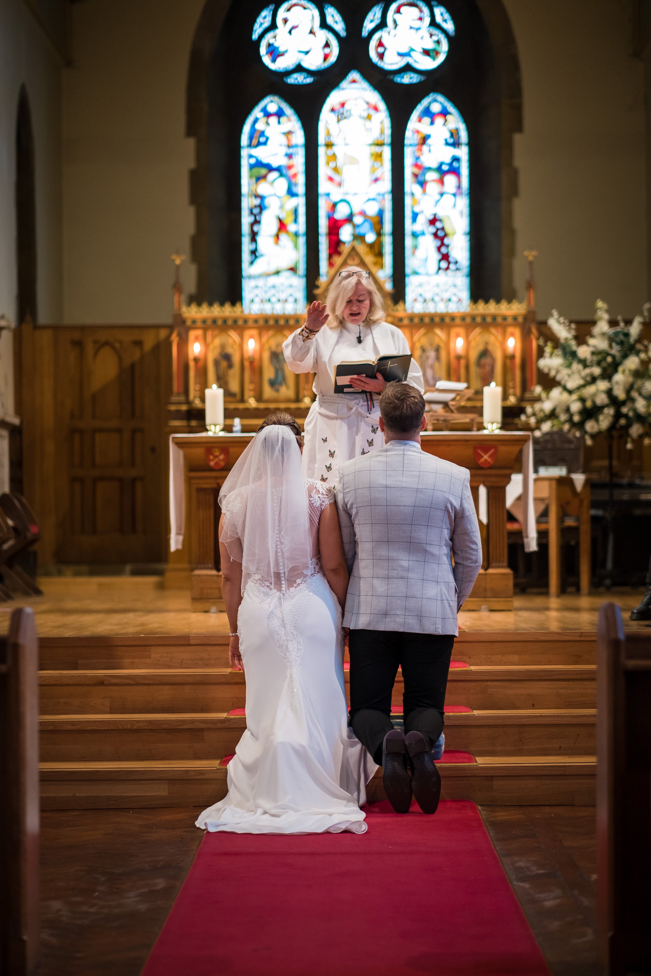 Sarah and Rob kneel before the Vicar as she prays over them.