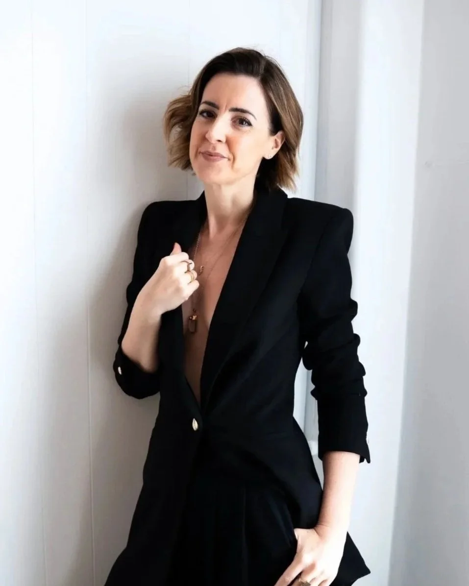 Lisa Moore, founder of House of Soul Sovereignty, wearing a black blazer leaning against a wall smiling