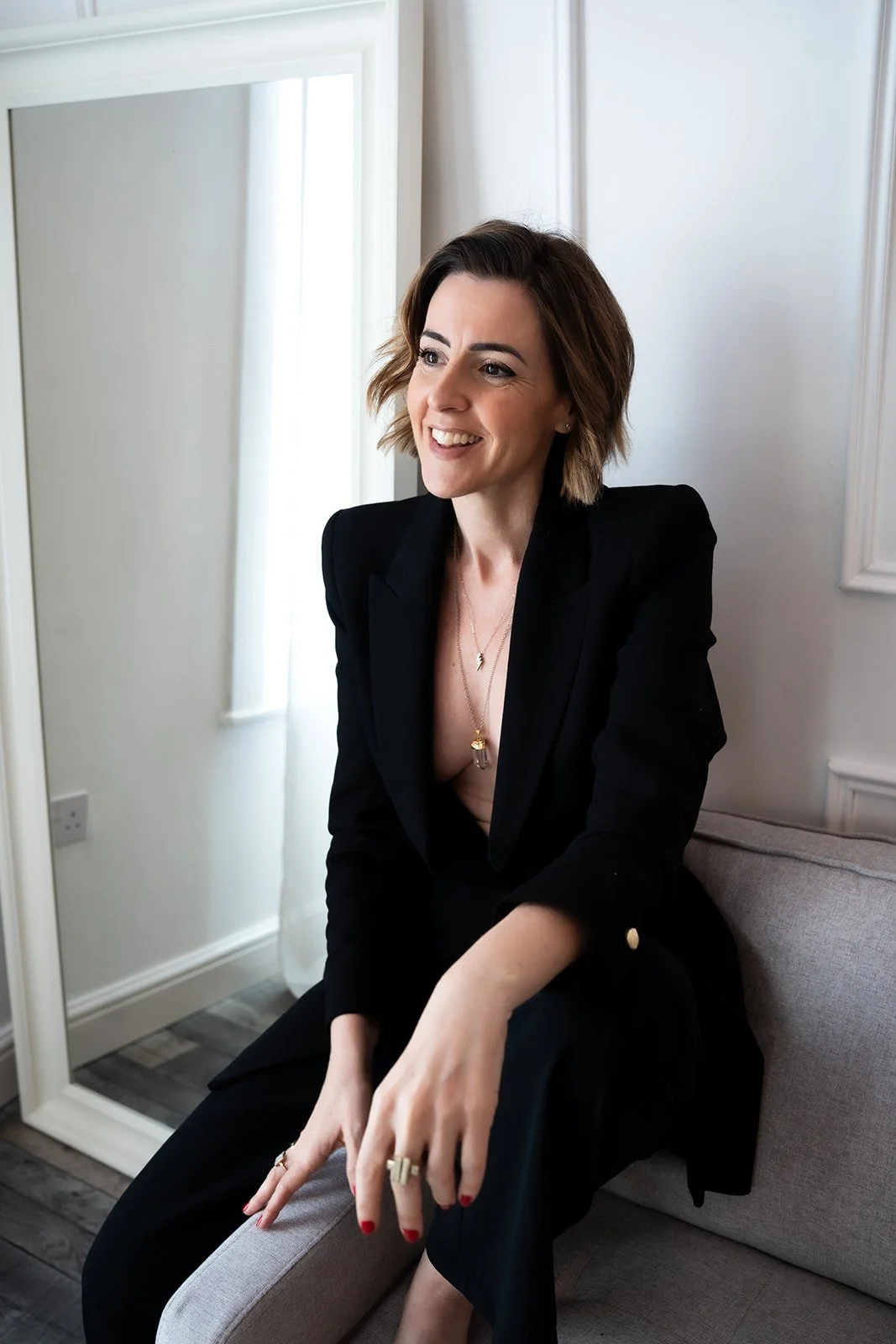 Lisa Moore, Sovereign Frequency Architect, seated in a black blazer, smiling warmly in a bright natural light setting