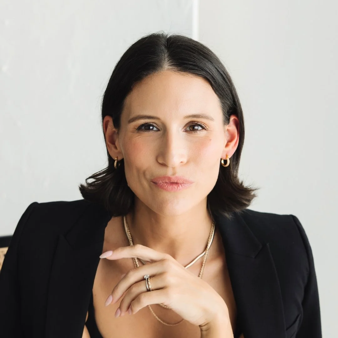 Kat, client of Lisa Moore, Sovereign Frequency Architect, looking directly at the camera with a calm and knowing expression, wearing gold hoop earrings and a black blazer