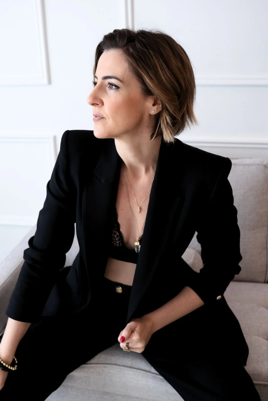 Lisa Moore, Sovereign Frequency Architect, seated in a black suit looking contemplatively to the side, embodying sovereign presence and quiet authority