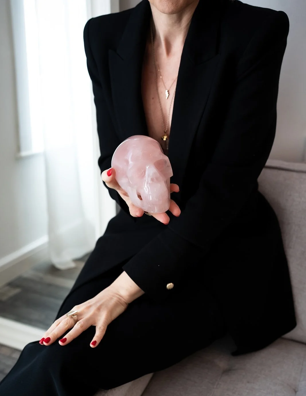 Lisa Moore, founder of House of Soul Sovereignty, wearing a black blazer and pants, holding a pink crystal skull sculpture in her right hand