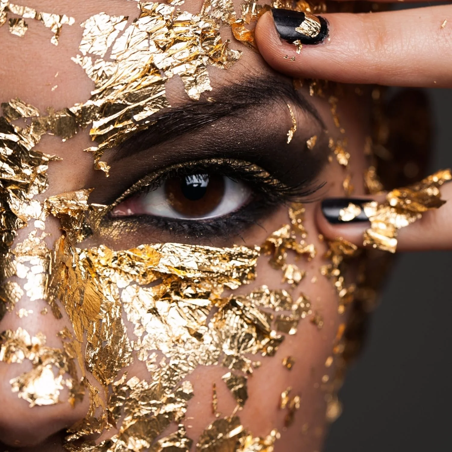 Close-up of a woman with gold leaf covering her face, one intense eye visible, black nails, embodying sovereign boundaries and divine creator power