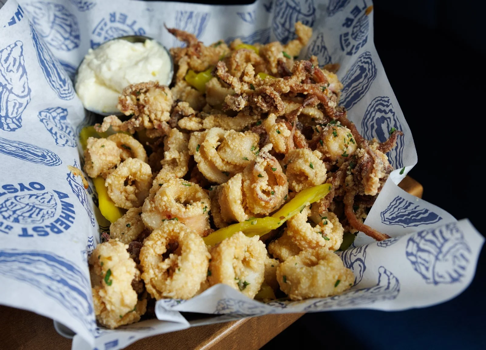 Crispy fried calamari with banana peppers and aioli in a basket lined with Amherst Oyster Bar paper