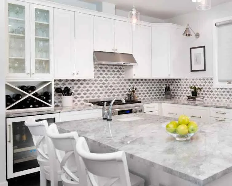 Modern white kitchen with marble island counter, white cabinets, a built-in wine rack, stainless steel appliances, and a bowl of green apples.