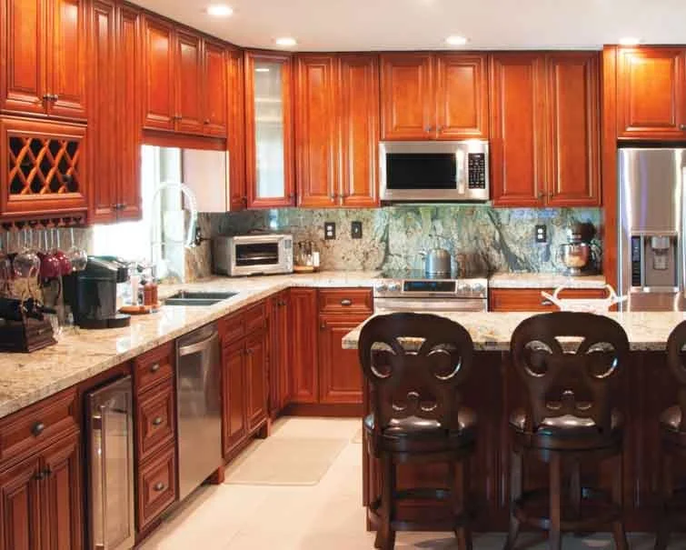 Kitchen with wooden cabinets, marble countertops, stainless steel appliances, and a breakfast bar with three black chairs.