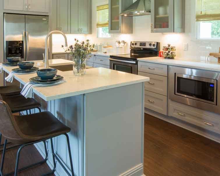 Modern kitchen with light gray cabinets, stainless steel appliances, a center island with bar stools, and a white countertop.