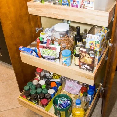 Open kitchen pantry drawer filled with snacks, canned goods, condiments, and bottles of beverages.