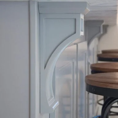 Close-up of a light blue wooden counter or bar with decorative support brackets and wooden stools with black metal legs in a modern interior.
