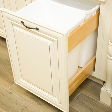 A partially assembled white kitchen cabinet with a door and wooden drawers, positioned beside a white countertop with a drawer, on a wood floor.