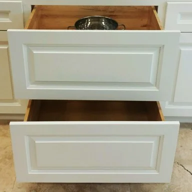 Two white kitchen cabinet drawers open, showing the empty interior and one has a black bowl inside.