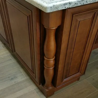 Close-up of a wooden kitchen island with a granite countertop and decorative supporting leg.