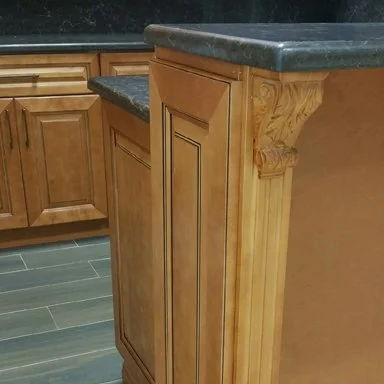 Close-up of a wooden kitchen cabinet with a dark stone countertop and decorative corbel support.