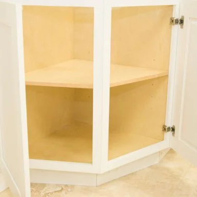Empty kitchen corner cabinet with two glass doors and light-colored wood shelves.