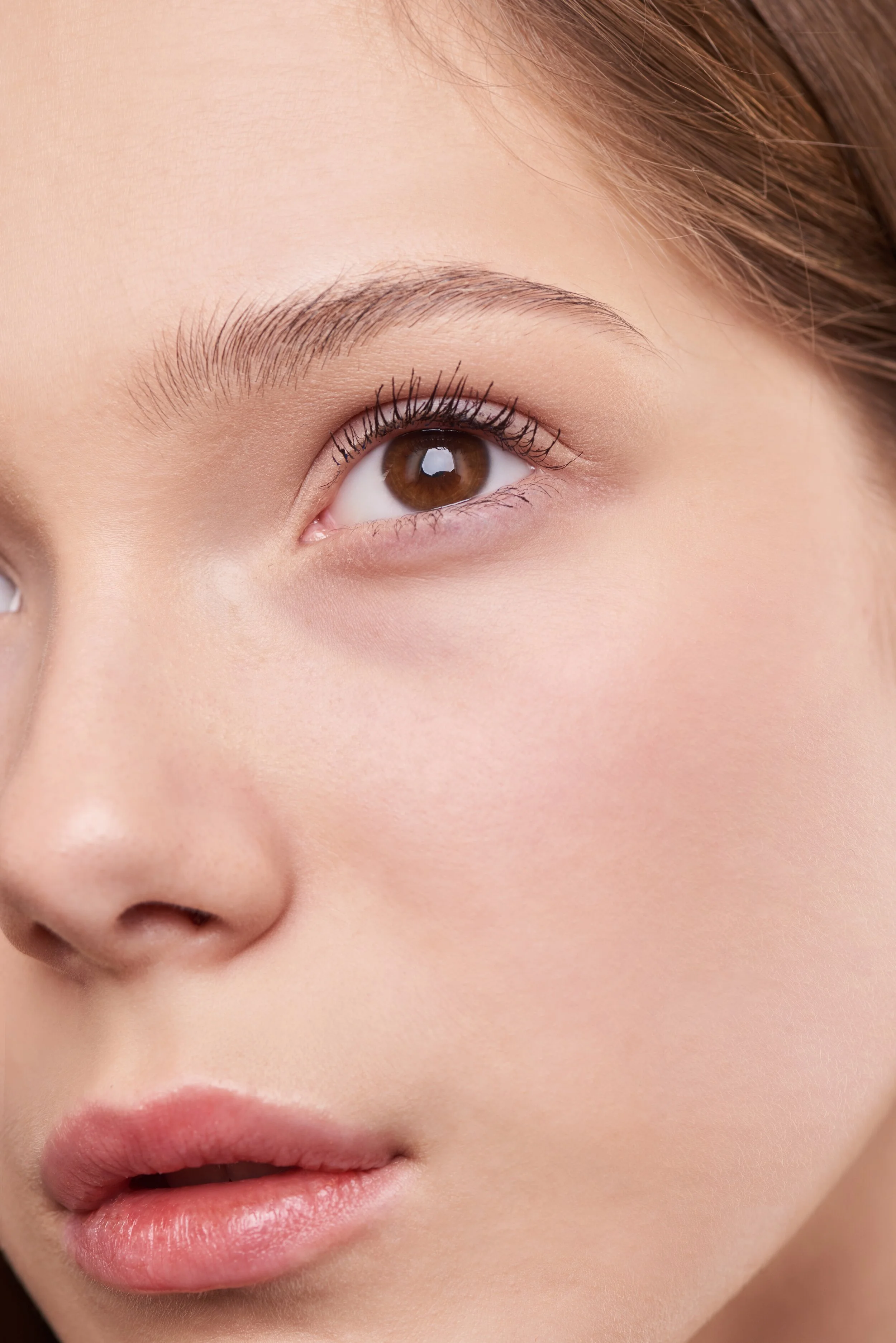 Close-up of a woman's face, showing her brown eye, smooth skin, and pink lips.