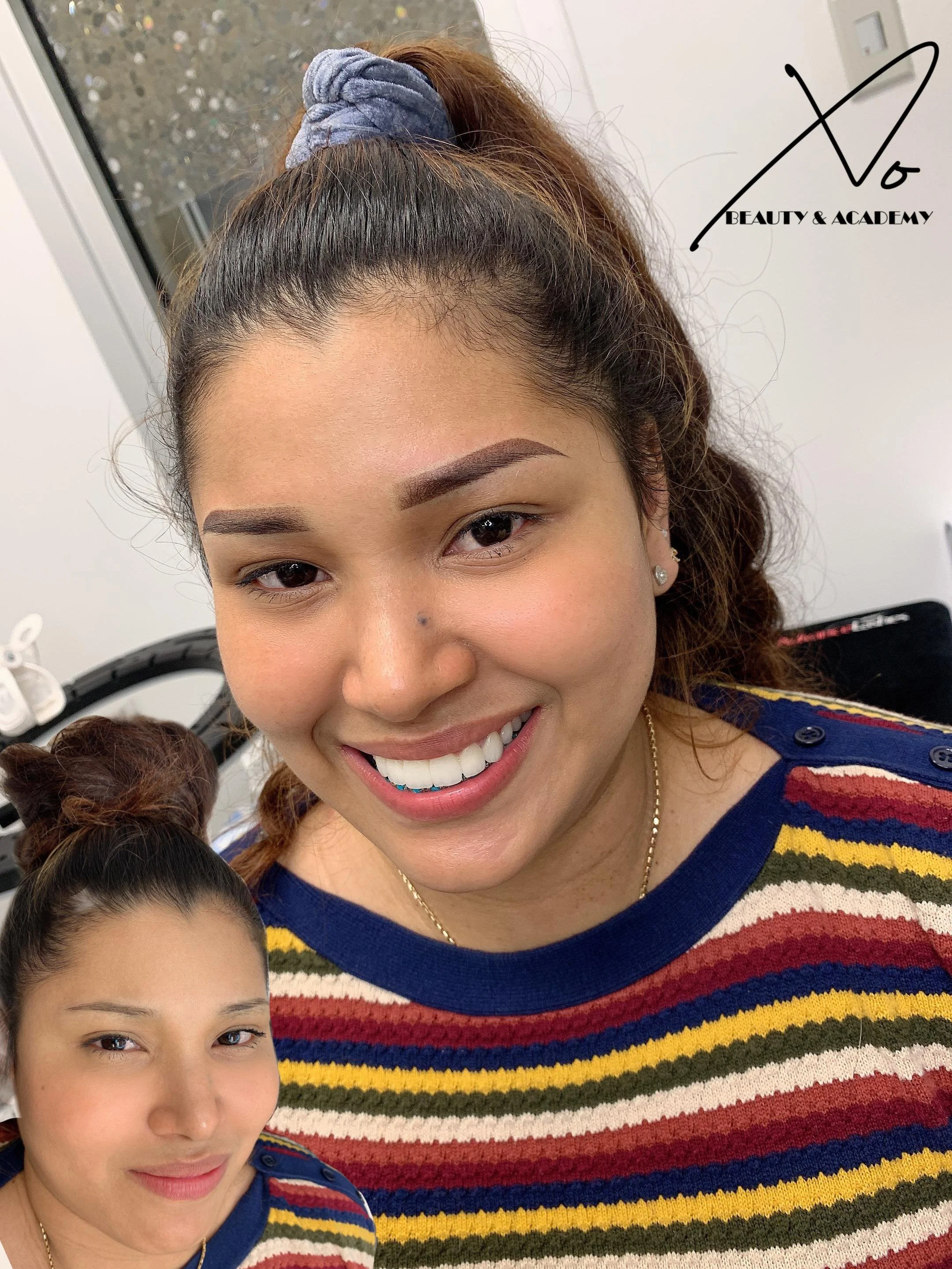 Close-up of a smiling woman with makeup, wearing a colorful striped sweater and a blue hair scrunchie, with a smaller version of herself in the lower left corner of the image.