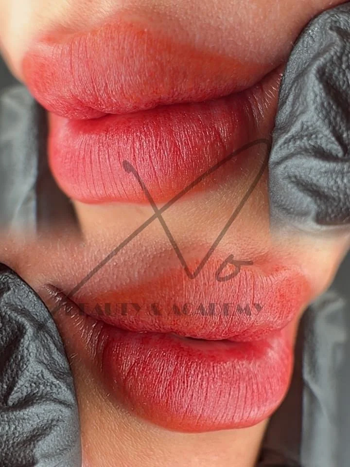 Close-up of a person's lips being tattooed with red lipstick color, using a tattoo needle, with gloves visible on the sides.