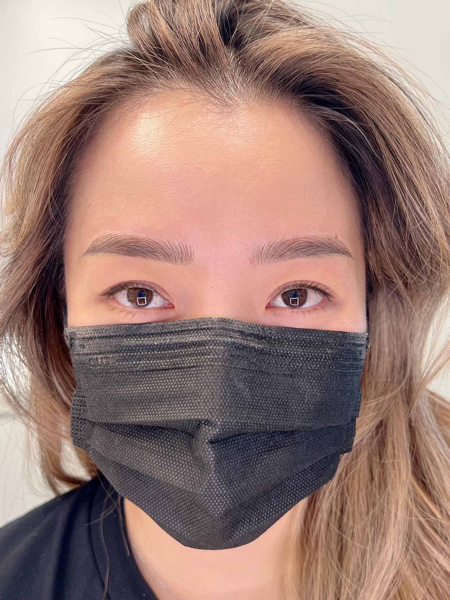 Close-up of a woman wearing a black face mask and with light brown hair.