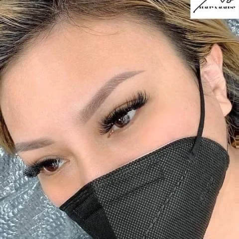 Close-up of a woman wearing a black face mask and eye makeup, including long eyelashes and well-defined eyebrows.