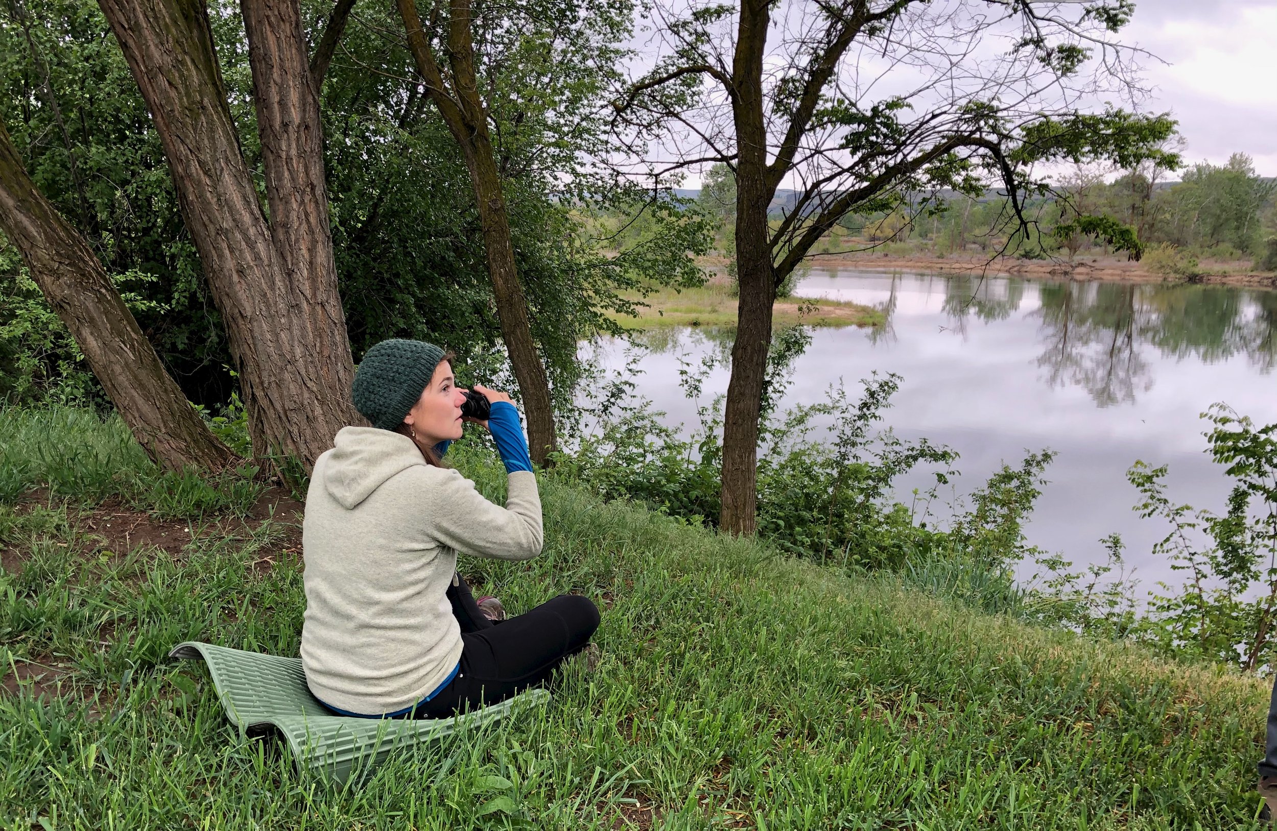Person sitting with binoculars near a pond.