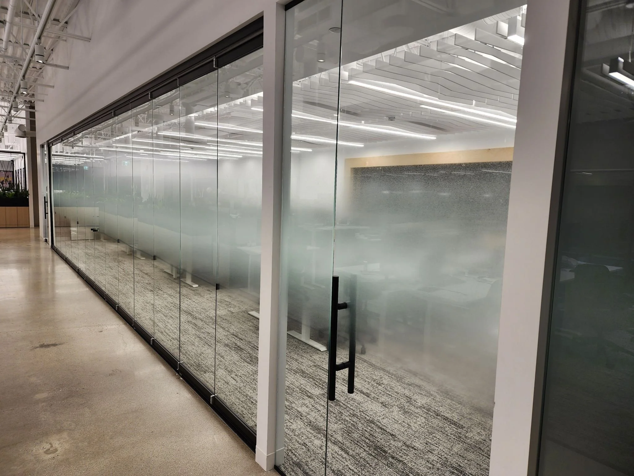 Modern office conference room with glass walls and frosted glass door, illuminated ceiling lights, and a patterned carpet.