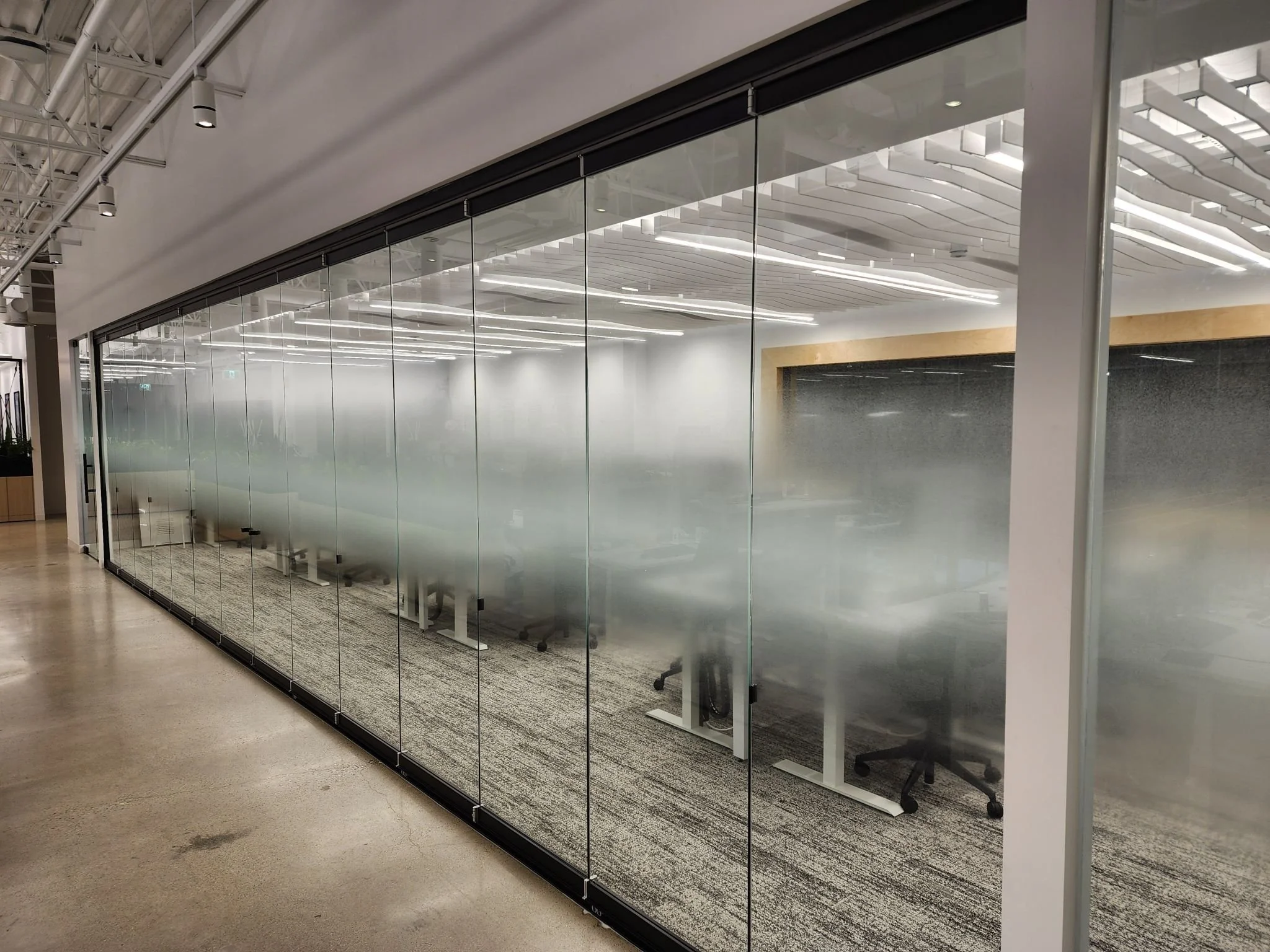 Empty modern conference room with frosted glass wall, office chairs, and contemporary ceiling lighting.
