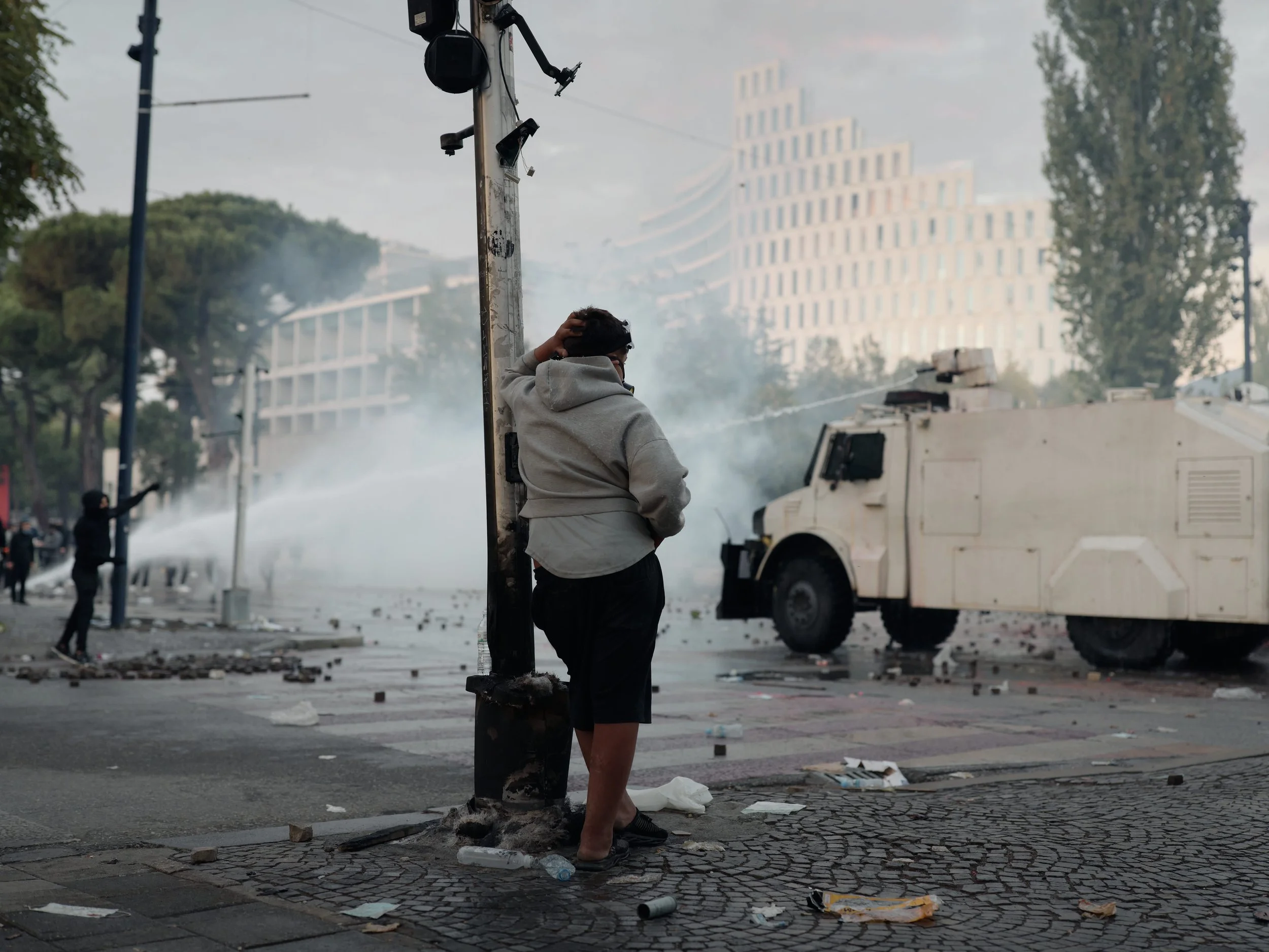 A young teenager watches the intense confrontation between police and demonstrators, as water cannons are deployed along the boulevard.
