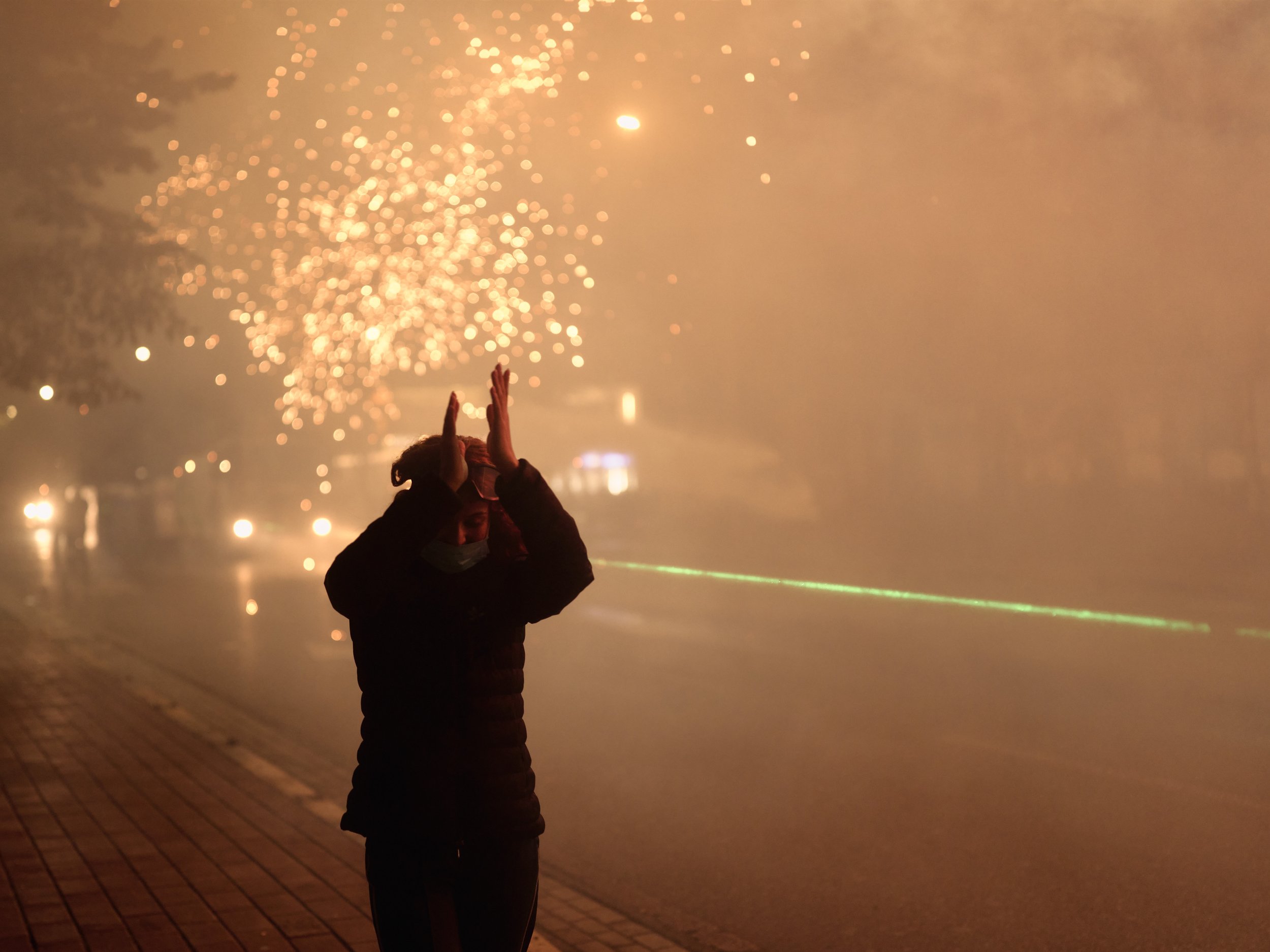 A demonstrator applauds after fireworks thrown by protesters force police officers to step back.
