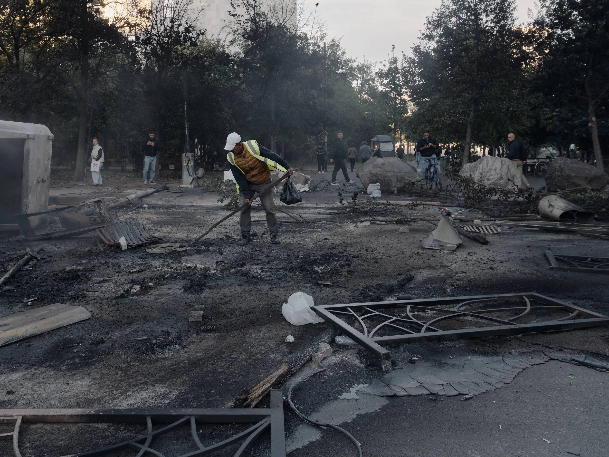 A municipal sanitation worker removes ash from a large fire where demonstrators burned rubbish bins and benches at the entrance to Skanderbeg Square, near Rruga e Durrësit.