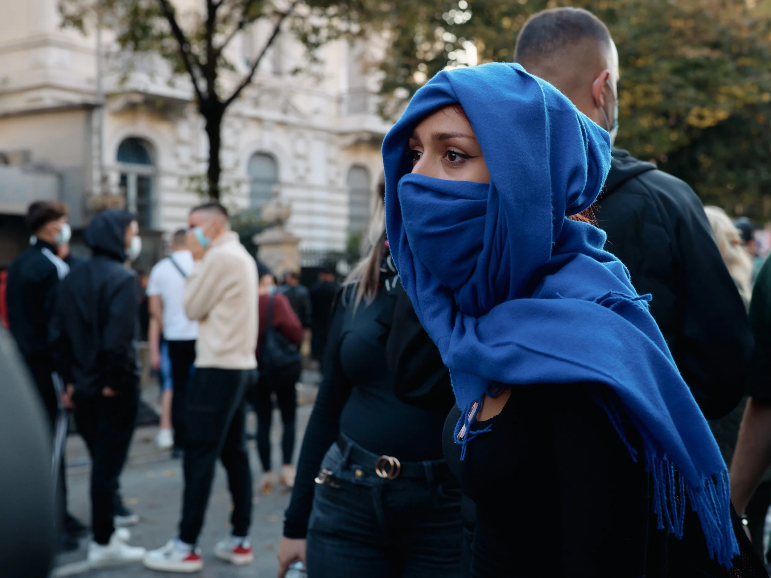 A young woman covers her face with a blue scarf to protect herself from tear gas.