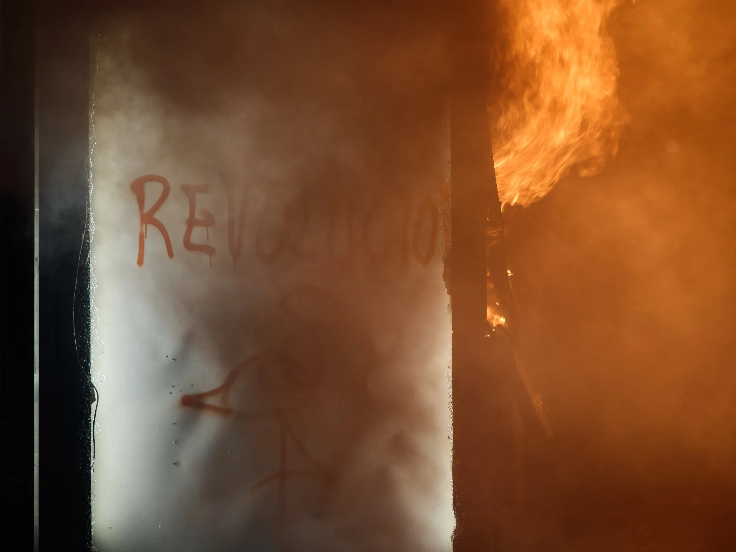 A bus stop burns in Tirana, marked with the word “Revolution” and the symbol of the Flamingo Revolution.