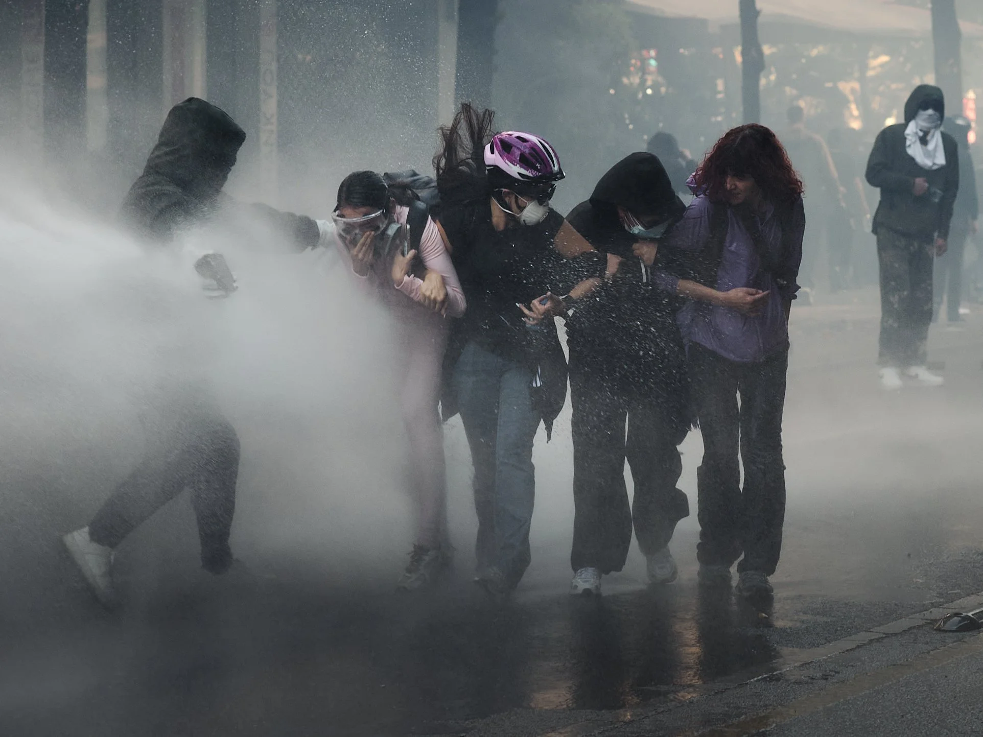 Four young women activists stand against the force of a water cannon as a man steps forward to shield them from the water on Rruga e Durrësit, Tirana.