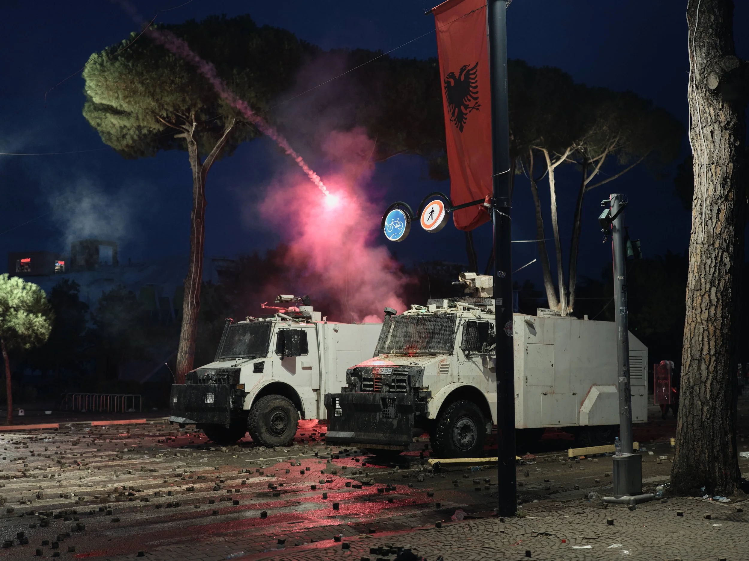A red flare strikes a water cannon, leaving a trail of smoke.