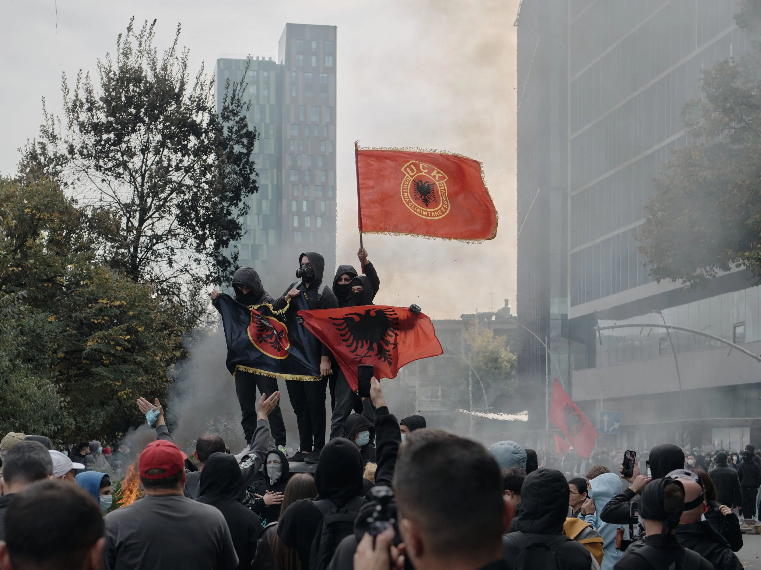 A group of students stand on top of a rubbish bin, waving Albanian and Kosovo Liberation Army (KLA/UÇK) flags.